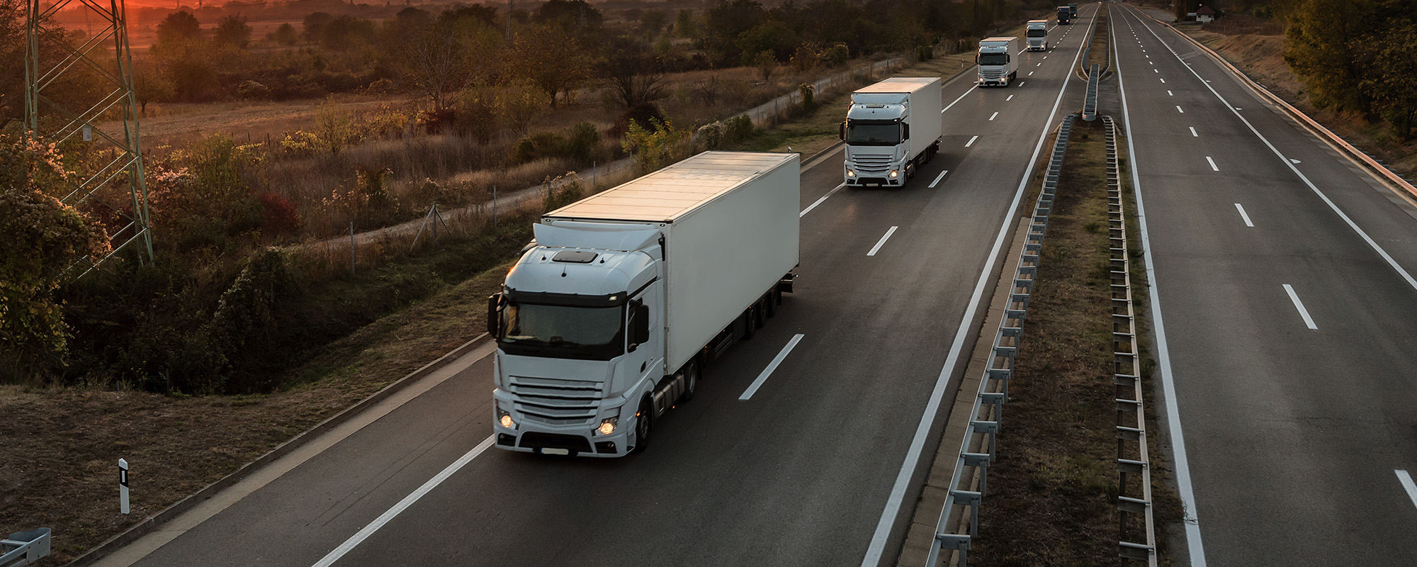 convoy of blue lorry trucks on a country highway under amazing orange sunset sky. highway transportation with white lorr