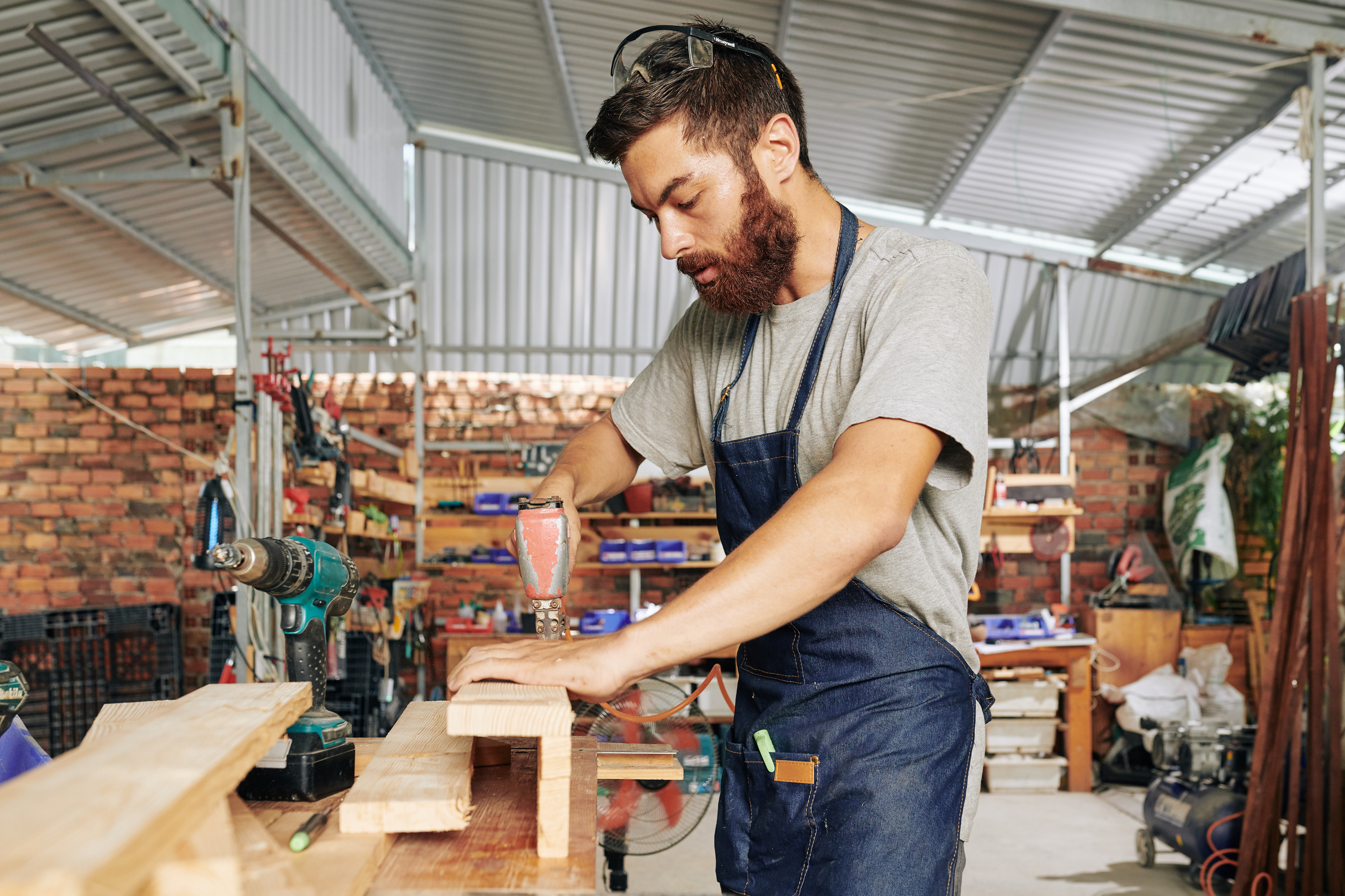 Serious bearded carpenter using drill when joining wooden blocks and making furniture